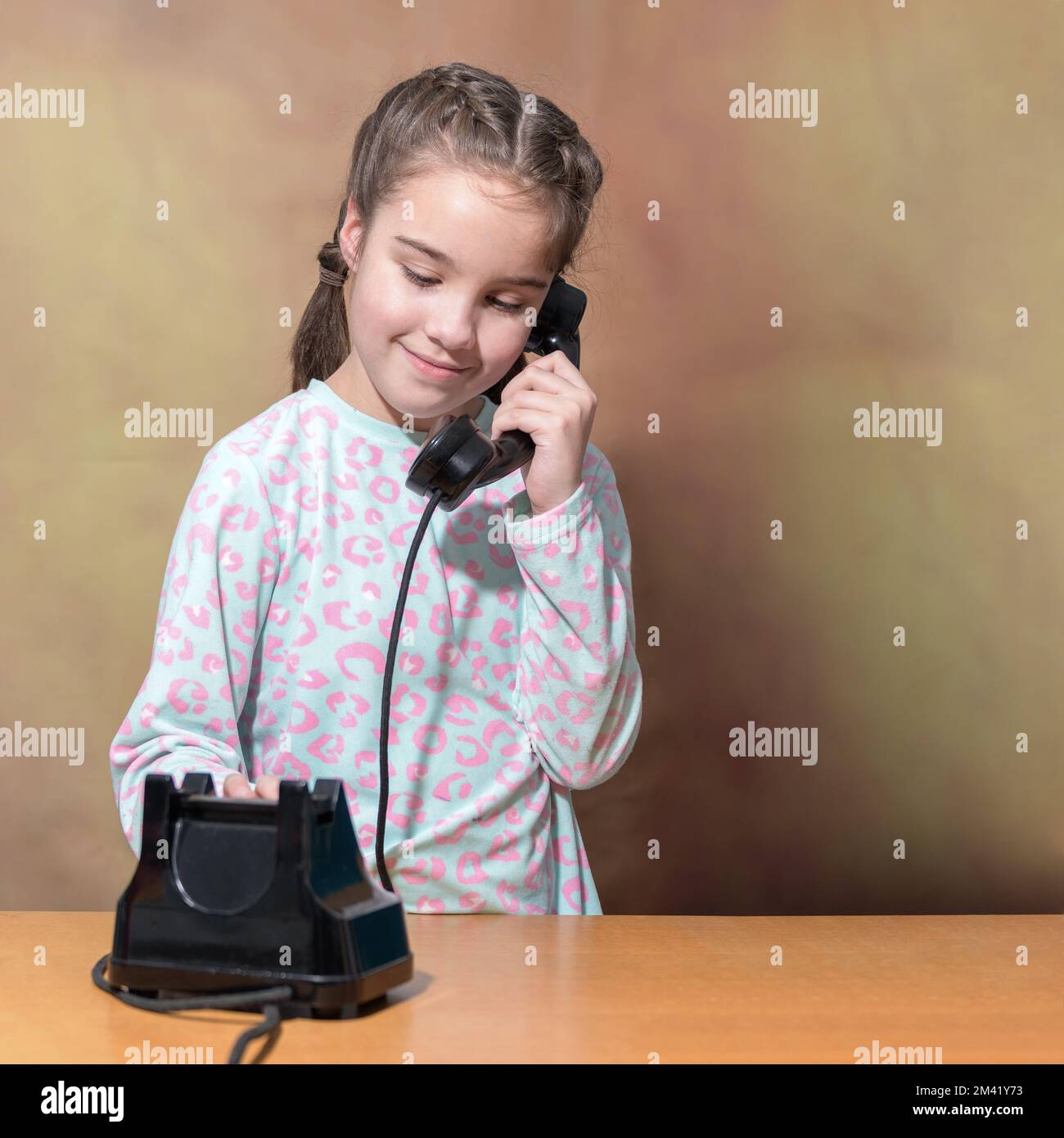 The teenage girl dials a number on an old telephone. Retro Portrait of a girl. Square format Stock Photo