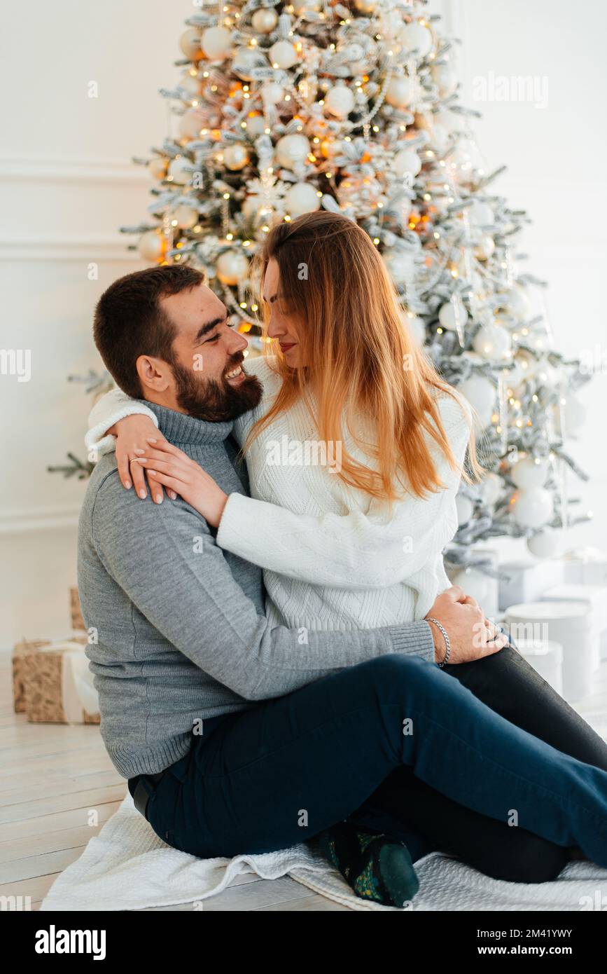 An attractive couple near Christmas tree and hugging. New Years atmosphere. Tender hugs near the Christmas tree of two people Stock Photo