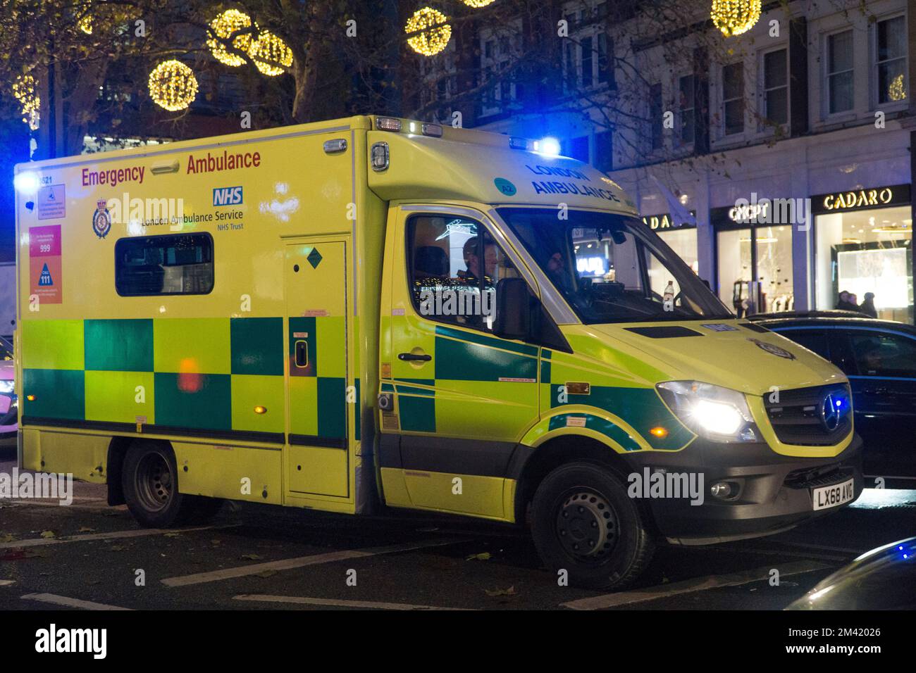 London, UK, 17 December 2022: An emergency ambulance makes it's way through heavy traffic in Knightsbridge, with Christmas lights in the background. In England and Wales ambulance drivers from the GMB, Unison and Unite unions are due to strike on 21 December in a dispute over pay. Anna Watson/Alamy Live News Stock Photo