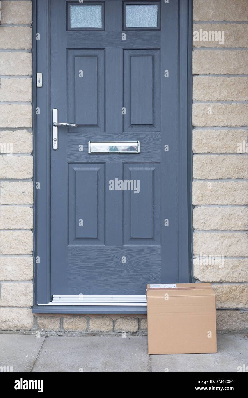 Small cardboard parcel left on the doorstep. Grey door and doorway. Courier delivery parcel. Stock Photo