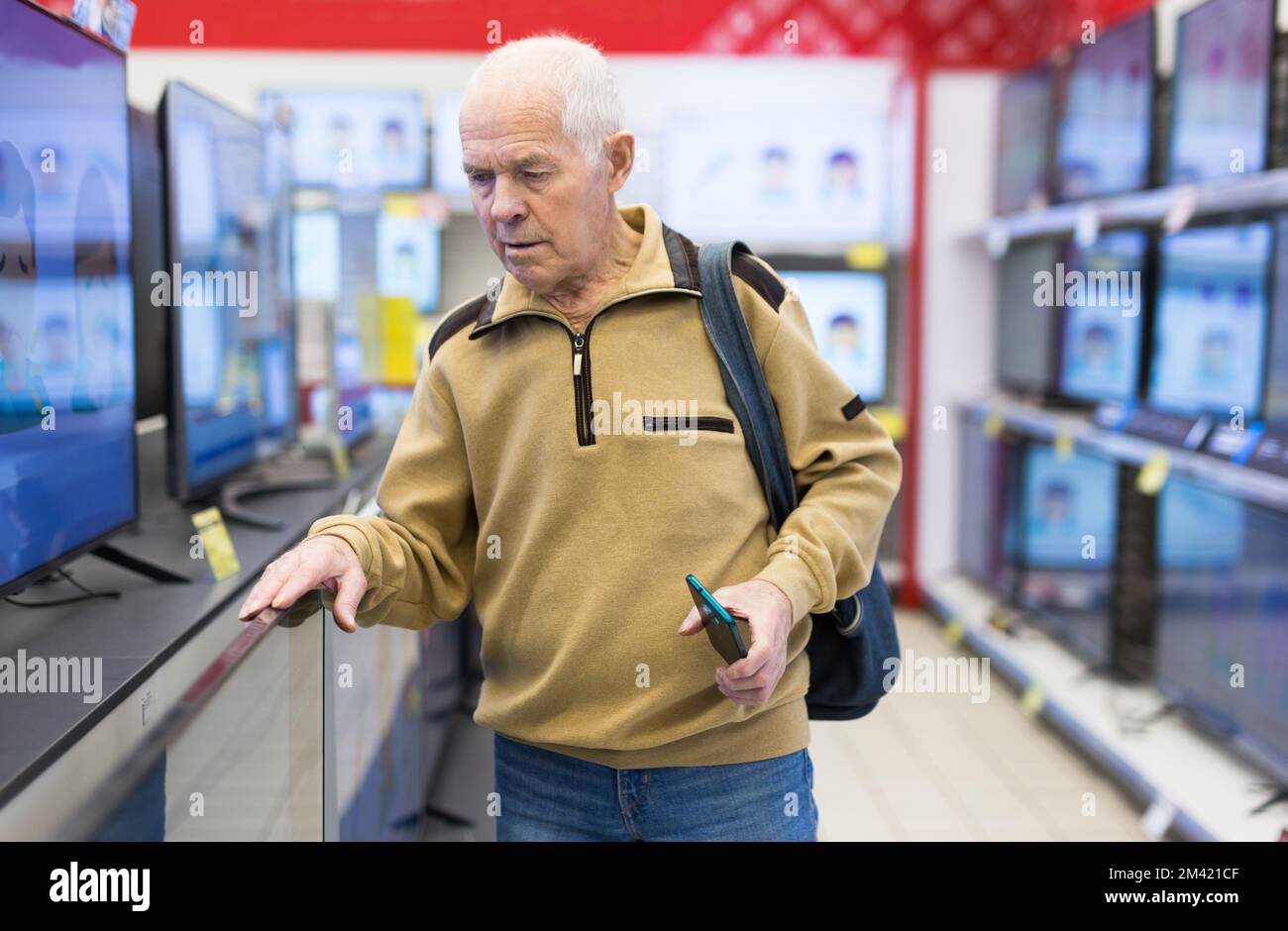 senor man pensioner buying modern digital televisor with smart tv in showroom of digital electronic goods store Stock Photo
