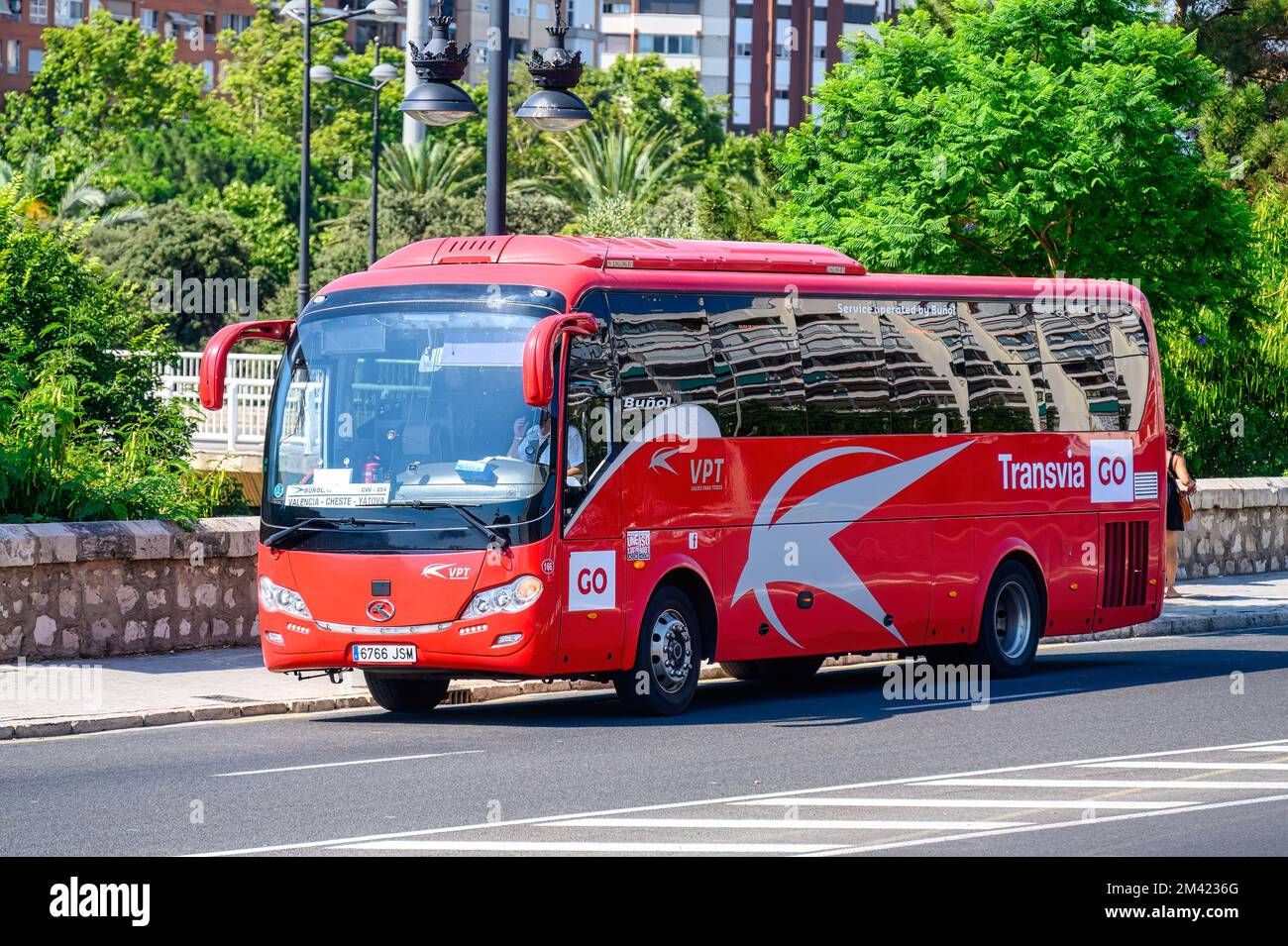 Passenger bus driving on a city avenue. The vehicle has inscriptions reading 'Viajes Para Todos', 'Transavia Go', and 'Buñol' Stock Photo