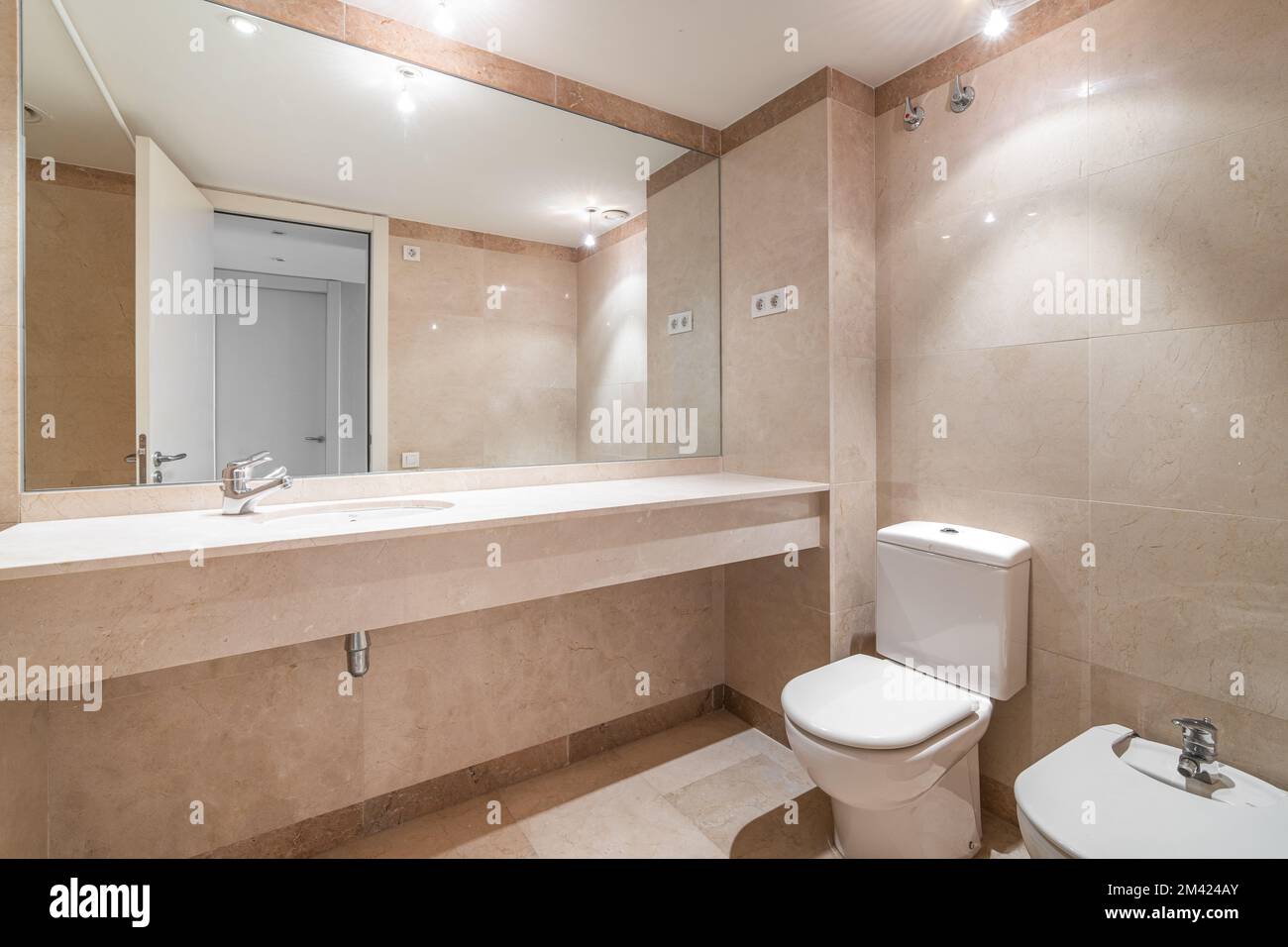 Modern spacious bathroom with bright beige tiles, toilet, bidet and ...
