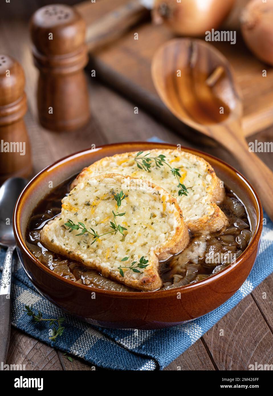 French onion soup with toasted cheese baguette garnished with thyme on a rustic wooden table background Stock Photo