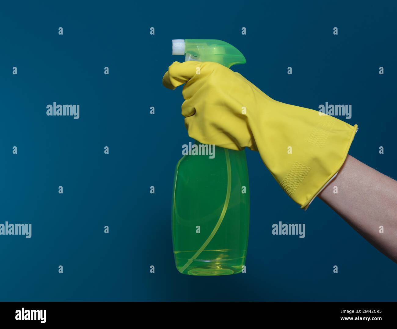 Hand in yellow rubber glove with a container of detergent. On blue ...