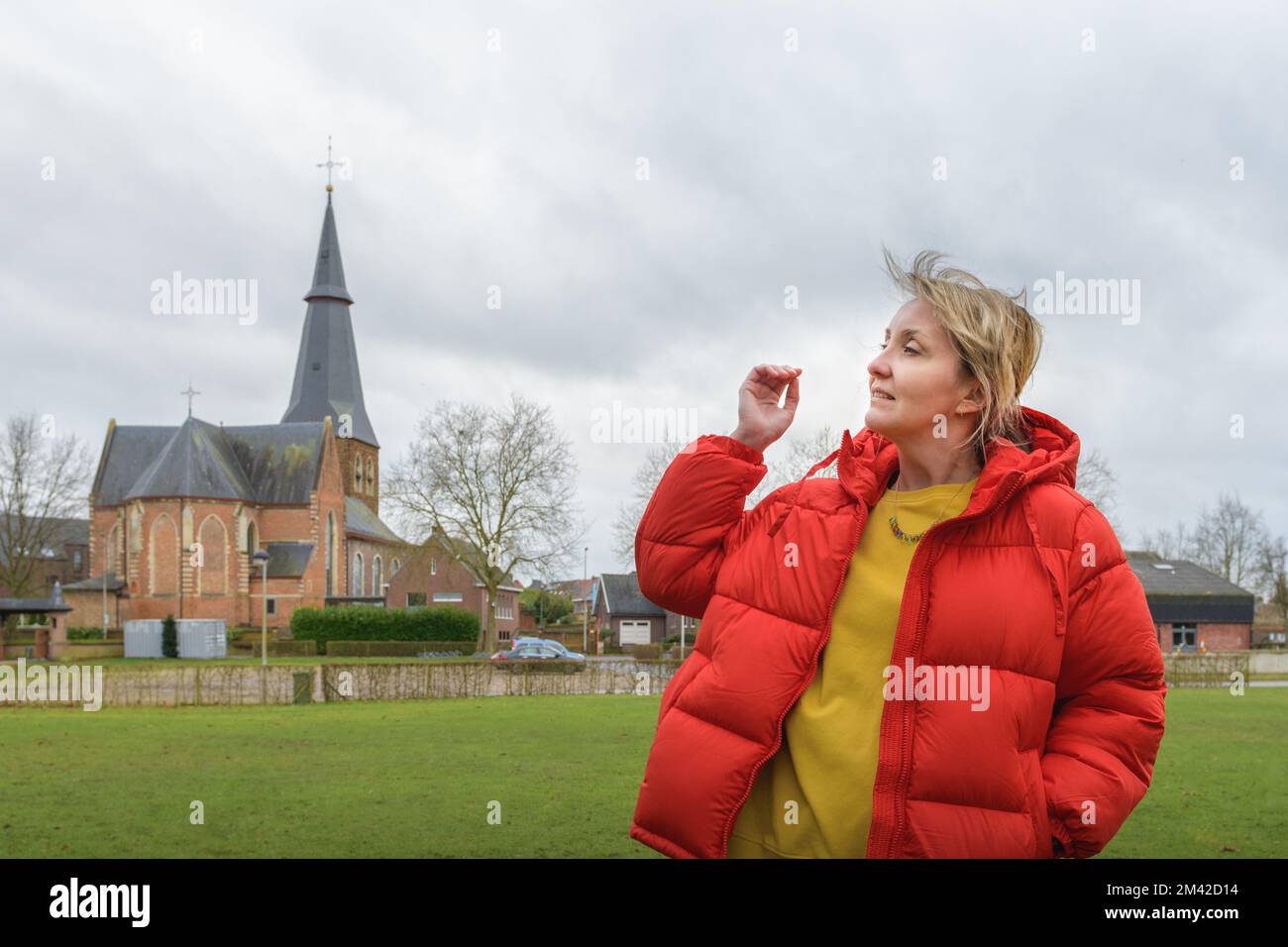 Portrait of woman against an old catholic church and cloudy sky. Woman in a red jacket Stock Photo