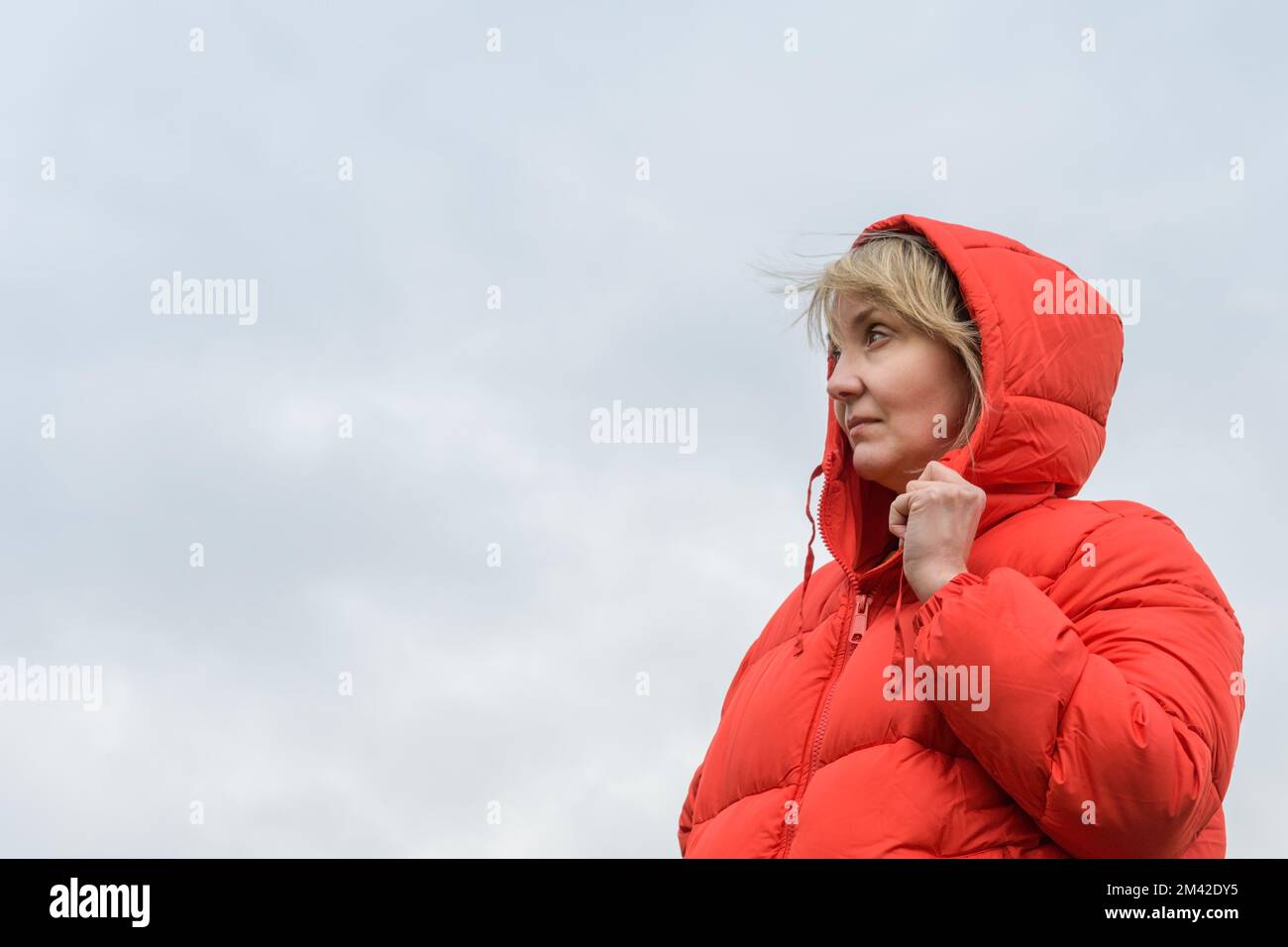 Woman in a red jacket. Portrait against a cloudy sky. copy space Stock Photo