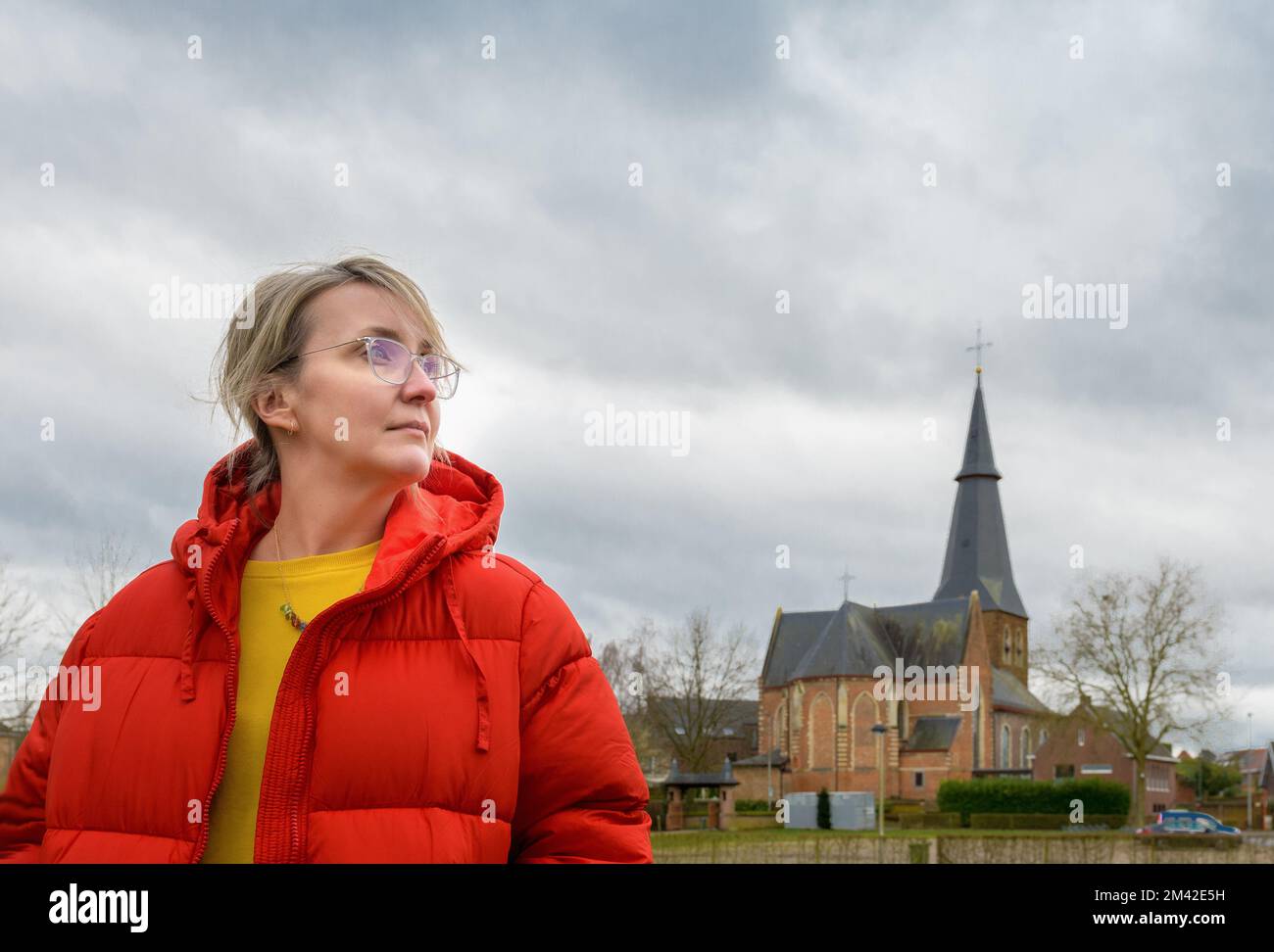 Woman in a red jacket. Portrait against an old catholic church and cloudy sky Stock Photo