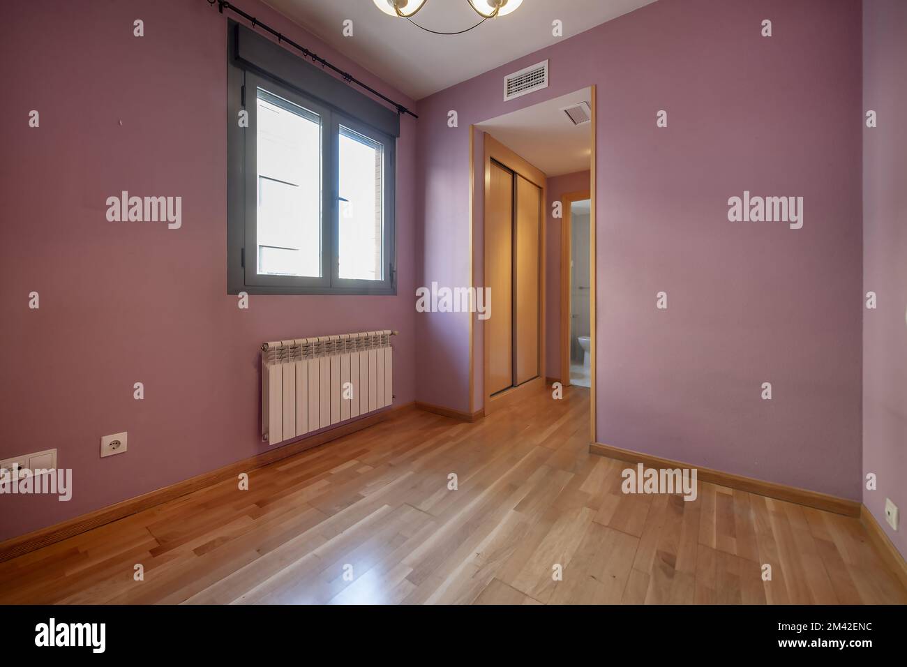 Empty bedroom with fuchsia painted walls, an antechamber with a sliding-door wardrobe, and access to an en-suite bathroom Stock Photo