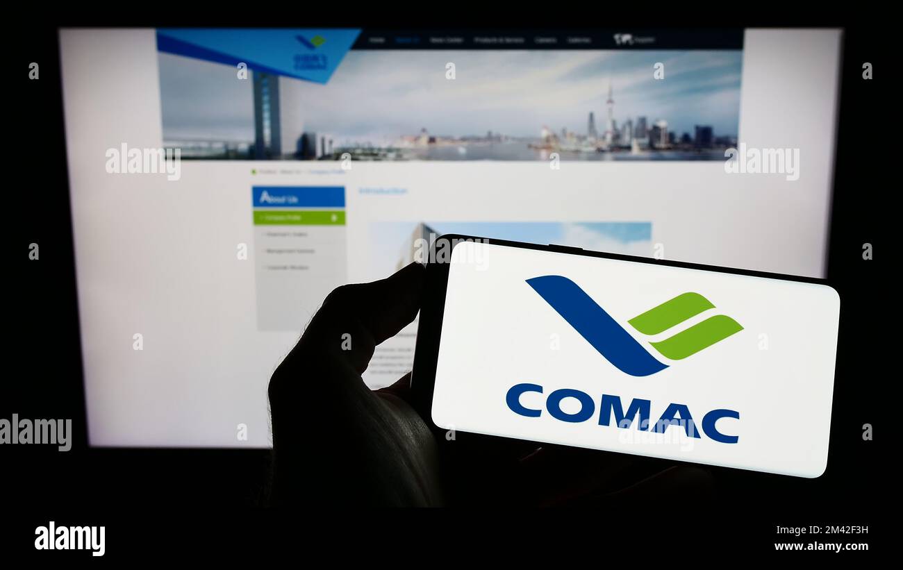 Person holding mobile phone with logo of Commercial Aircraft Corporation of China (COMAC) on screen in front of website. Focus on phone display. Stock Photo