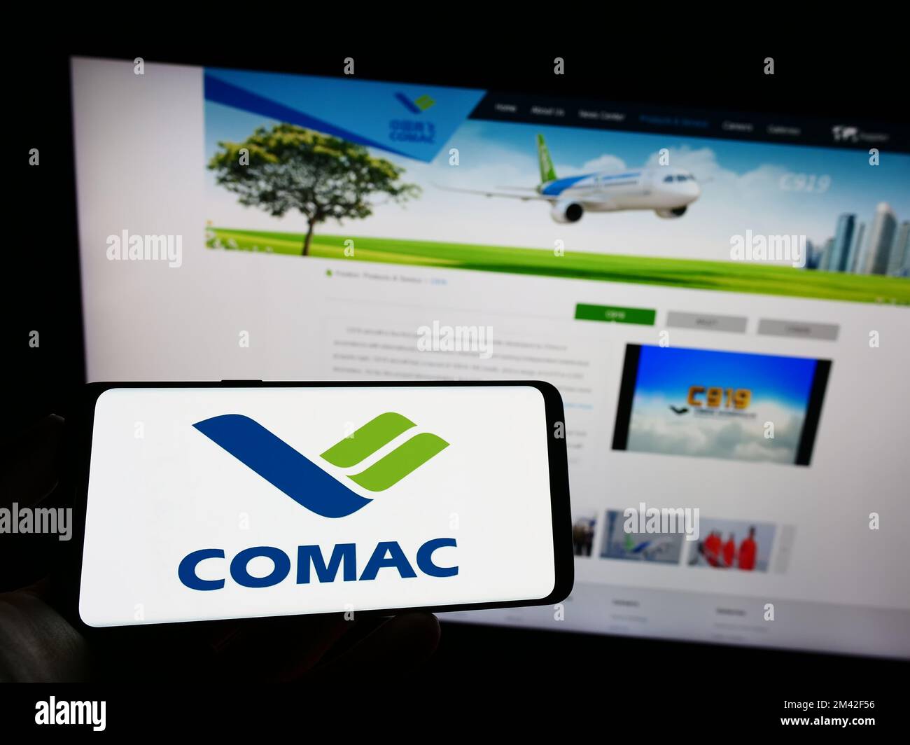 Person holding cellphone with logo of Commercial Aircraft Corporation of China (COMAC) on screen in front of webpage. Focus on phone display. Stock Photo