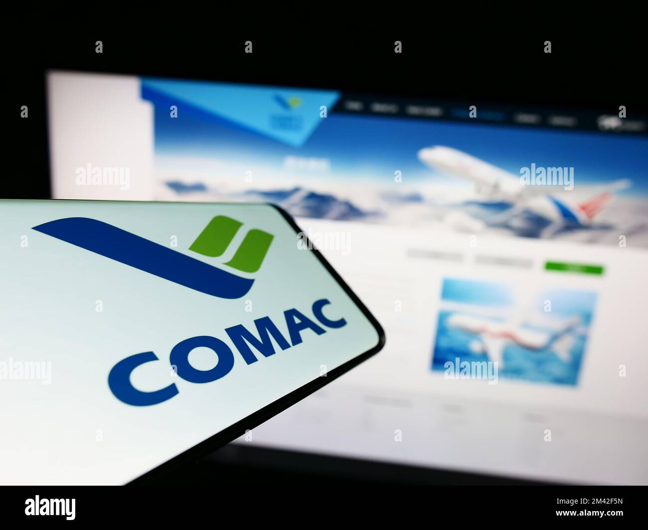 Mobile phone with logo of Commercial Aircraft Corporation of China (COMAC) on screen in front of website. Focus on center-right of phone display. Stock Photo