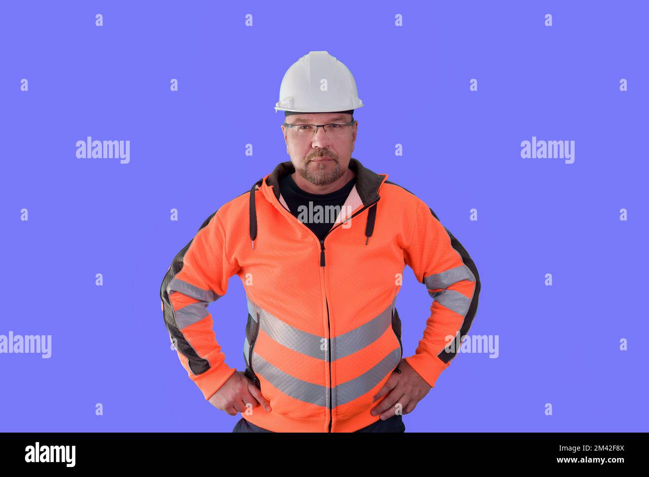 A male builder, in work clothes and a construction helmet, on a lilac ...