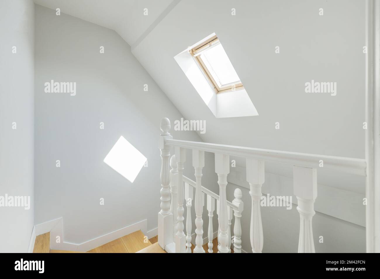 White painted wooden balustrade on the stairs of an attic with sloped ceilings and skylights with curtains Stock Photo