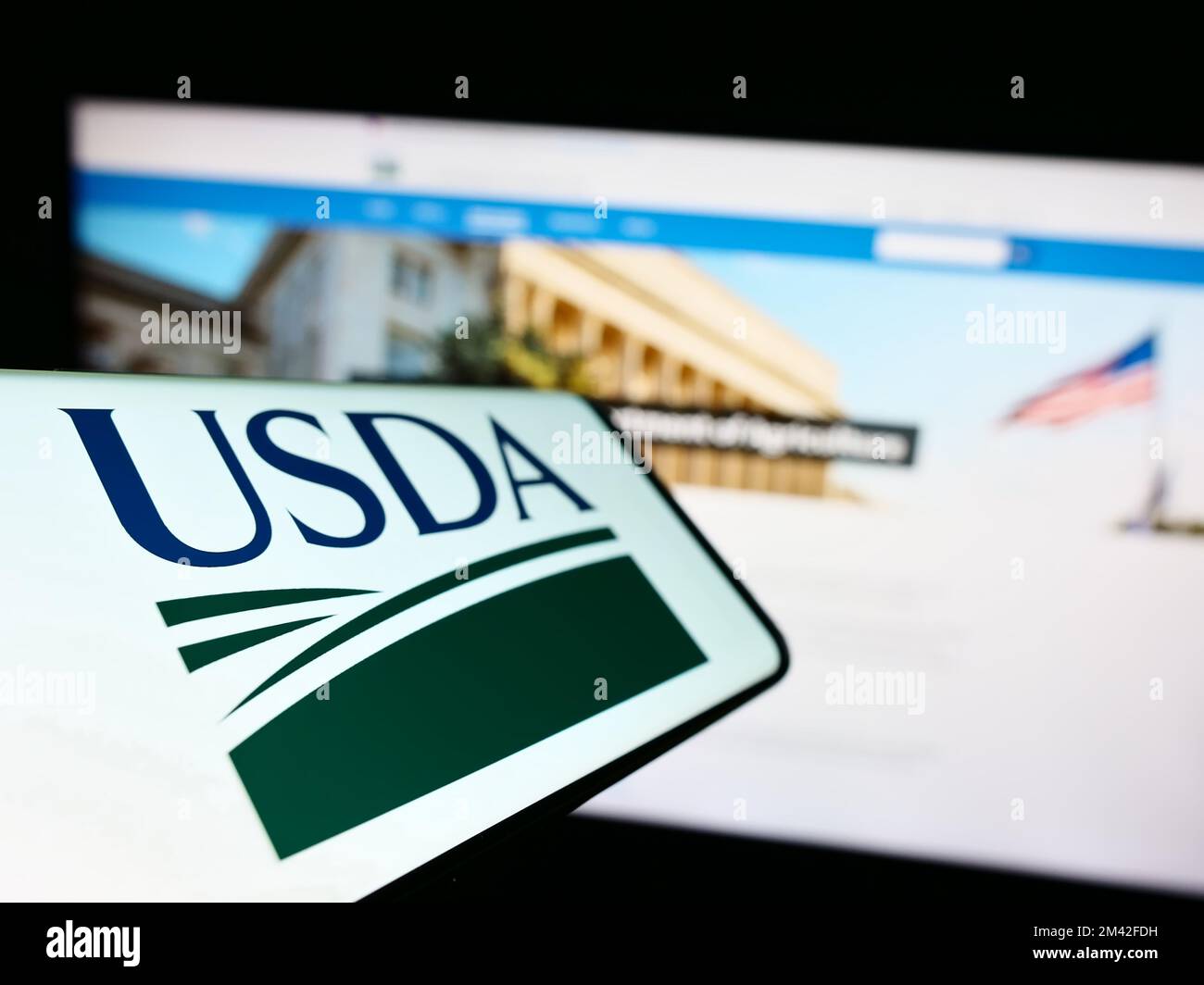 Smartphone with logo of United States Department of Agriculture (USDA) on screen in front of website. Focus on left of phone display. Stock Photo