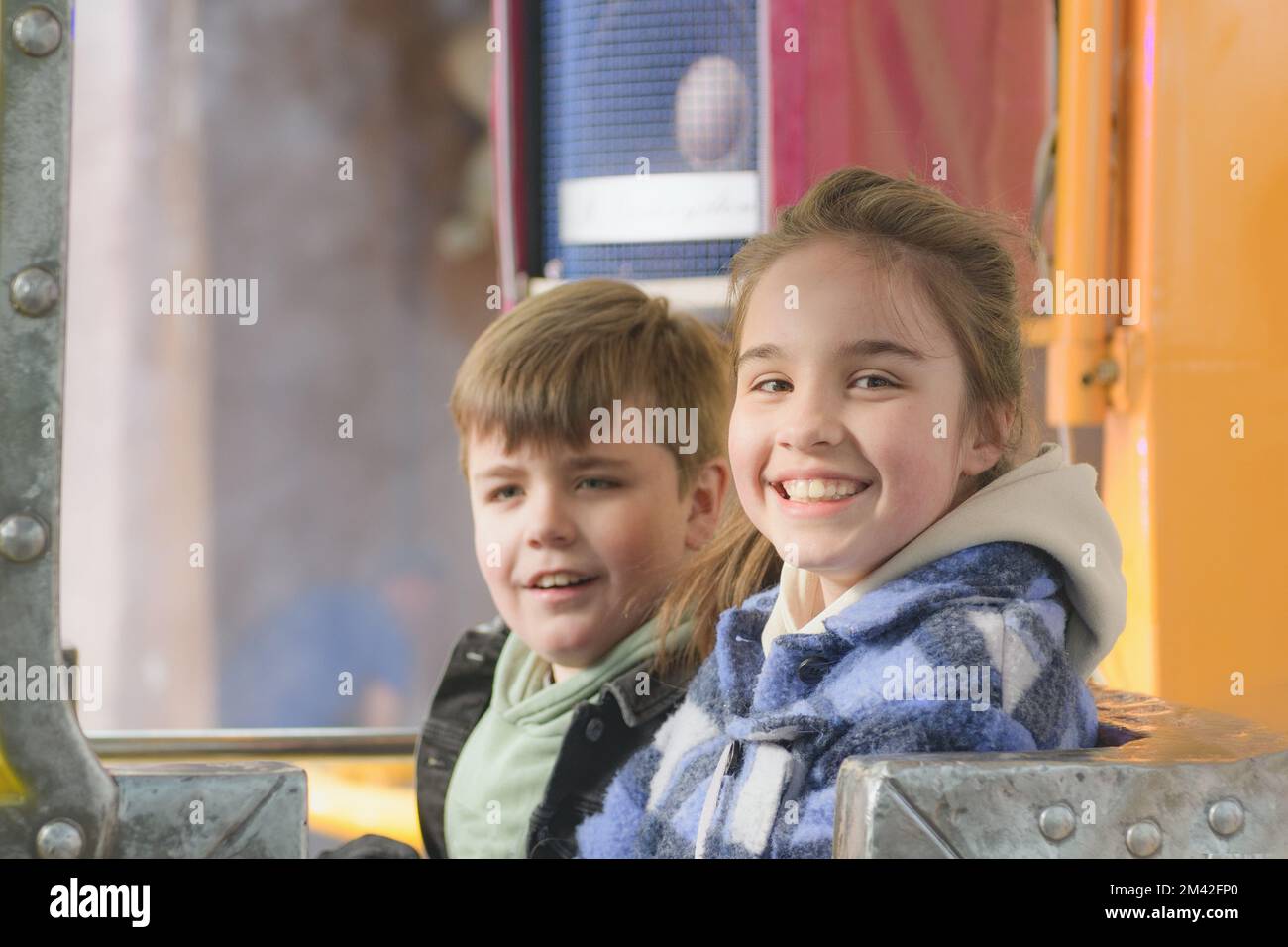 Girl and boy with positive emotions on the carousel in the amusement park. Stock Photo