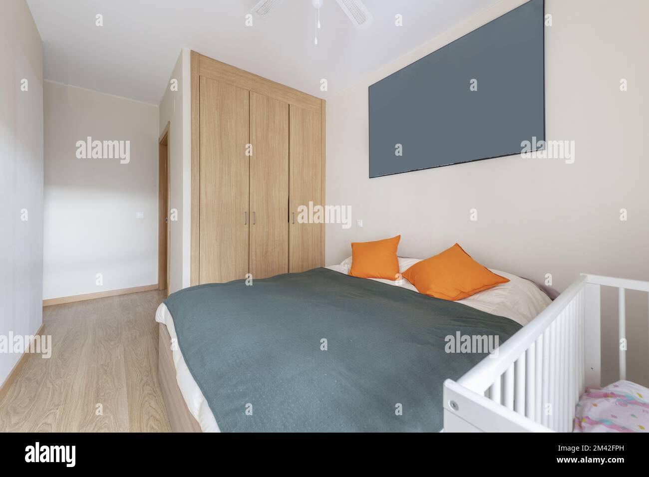 bedroom with a double bed and a white cot with a three-section built-in wardrobe and an en-suite toilet Stock Photo