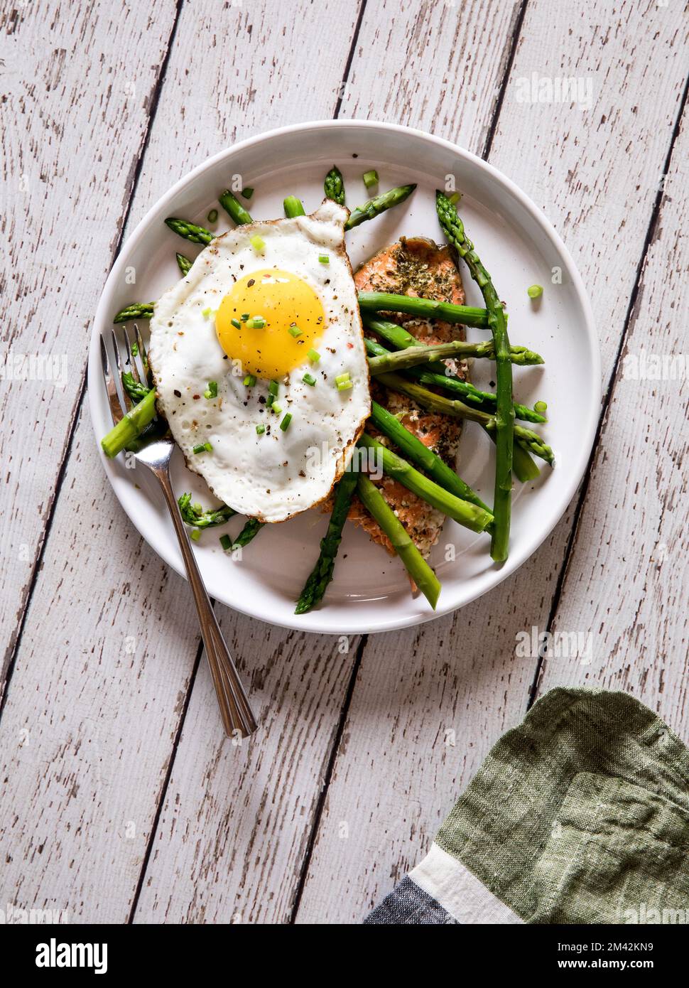 A plate of roasted salmon topped with steamed asparagus and a fried egg. Stock Photo
