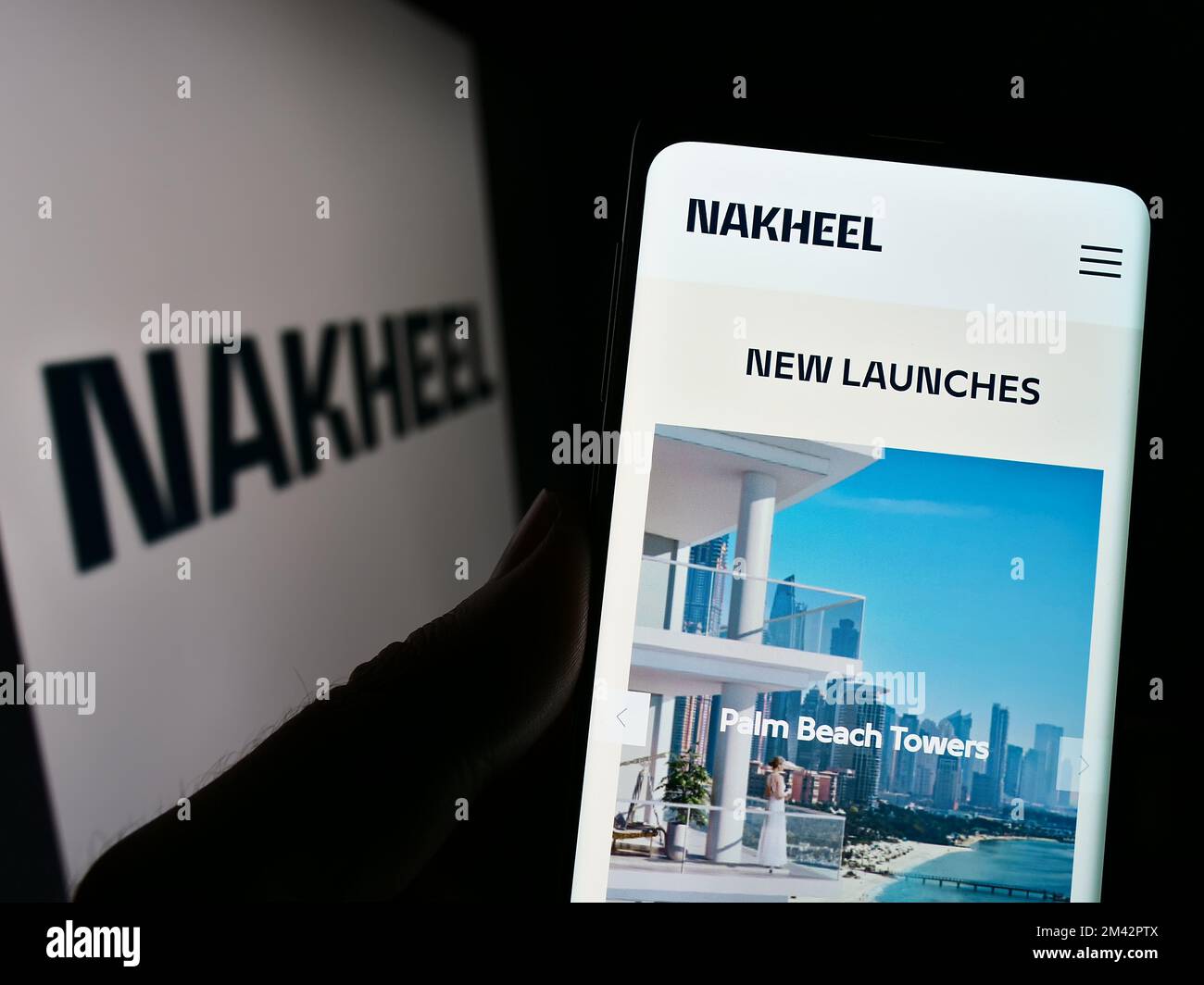 Person holding cellphone with webpage of Emirati real estate company Nakheel Properties on screen with logo. Focus on center of phone display. Stock Photo