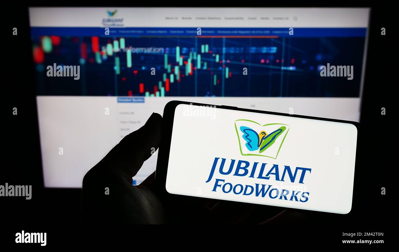 Person holding mobile phone with logo of Indian food company Jubilant FoodWorks Limited on screen in front of web page. Focus on phone display. Stock Photo
