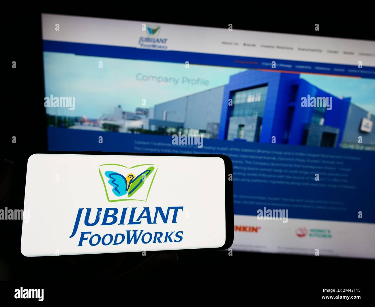 Person holding smartphone with logo of Indian food company Jubilant FoodWorks Limited on screen in front of website. Focus on phone display. Stock Photo