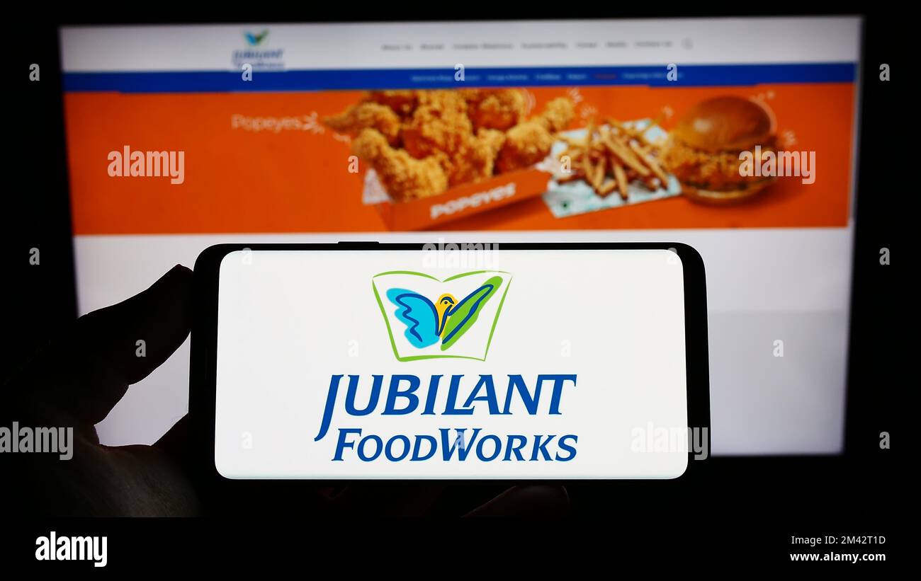 Person holding cellphone with logo of Indian food company Jubilant FoodWorks Limited on screen in front of webpage. Focus on phone display. Stock Photo