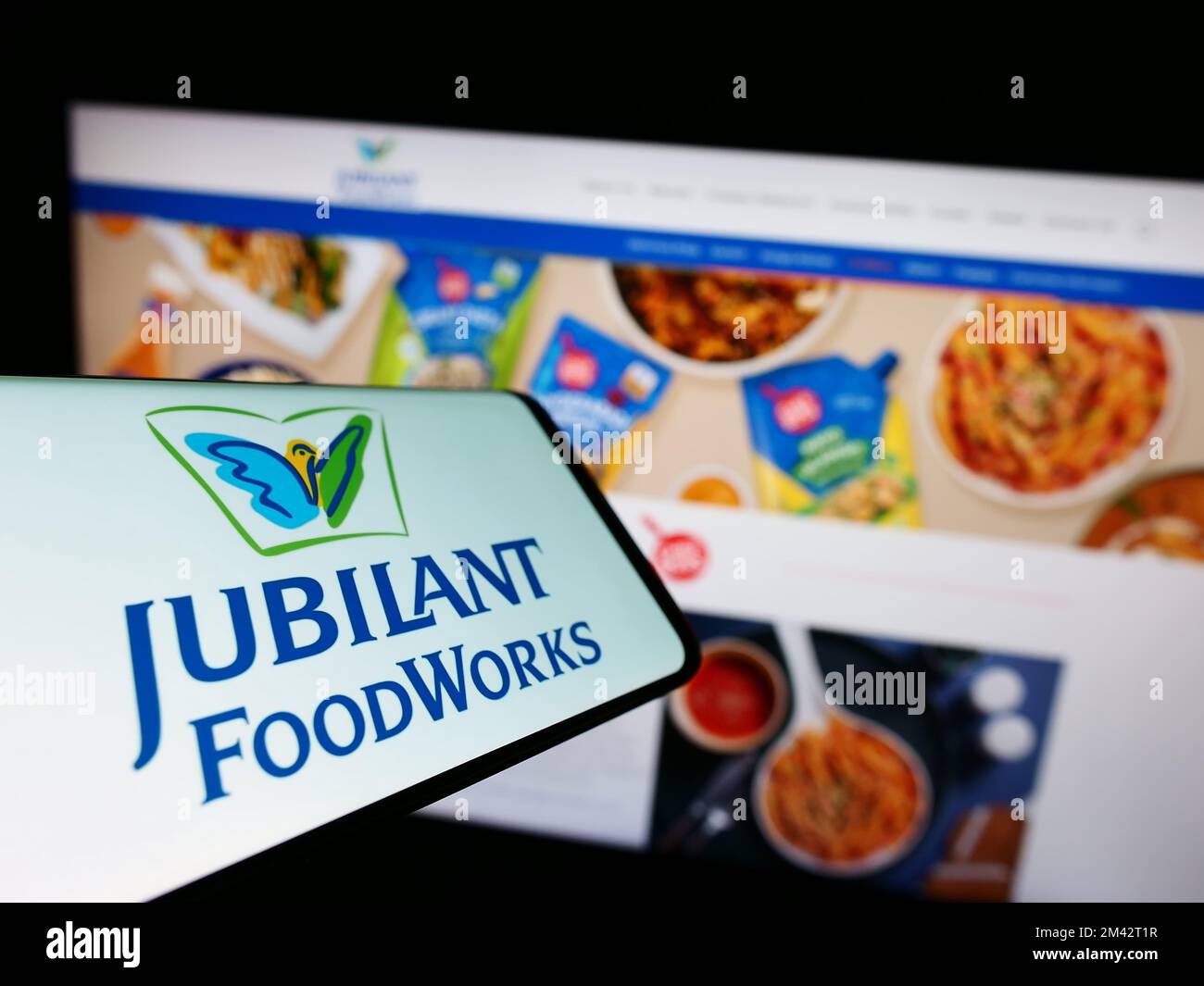 Cellphone with logo of Indian food company Jubilant FoodWorks Limited on screen in front of website. Focus on center-left of phone display. Stock Photo