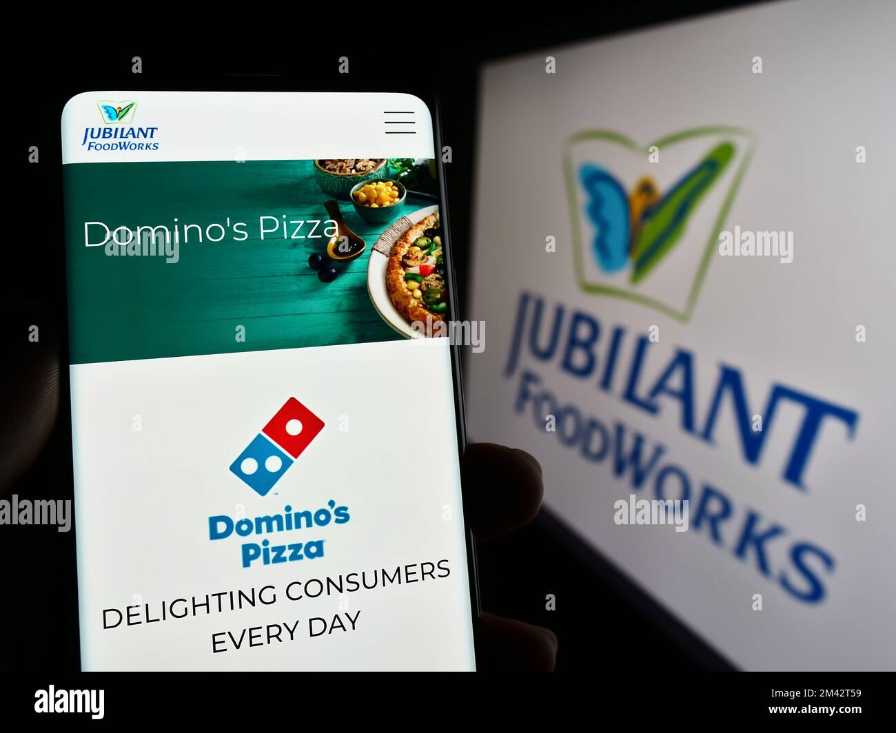 Person holding mobile phone with webpage of Indian food company Jubilant FoodWorks Limited on screen with logo. Focus on center of phone display. Stock Photo