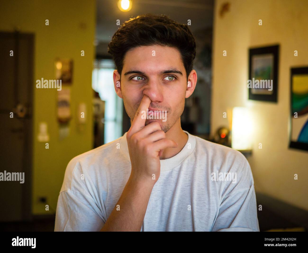 Handsome young man frowning and picking nose Stock Photo