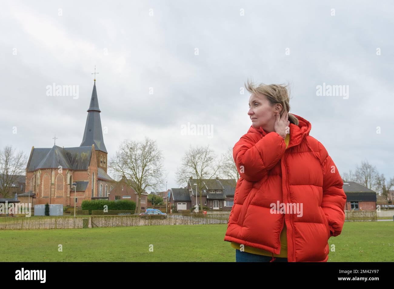 Before the rain. Portrait of woman against an old church and cloudy sky. Red jacket Stock Photo