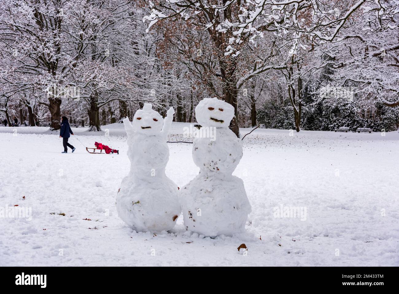 Zwei Schneemänner in einem Park eine Frau zieht einen Rodelschlitten mit einem Kind Stock Photo