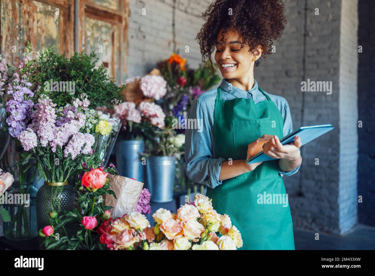 Young black woman wearing beige apron on flower shop background with