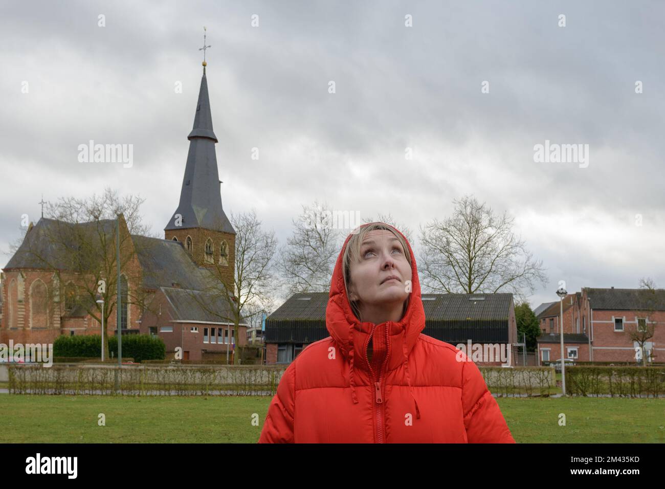 Waiting for the rain. Portrait of woman against an old church and cloudy sky. Red jacket Stock Photo