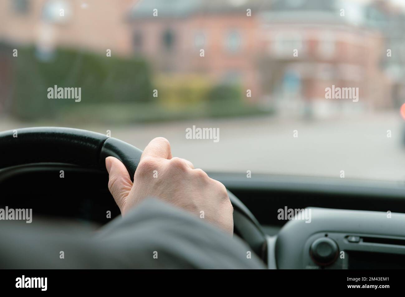 Hand of woman on a car steering wheel. Windshield and perspective of