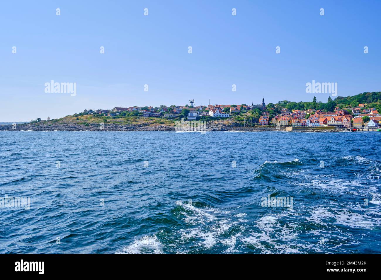 Wake behind a ship and picturesque view of the coastline of Gudhjem, Bornholm island, Denmark. Stock Photo