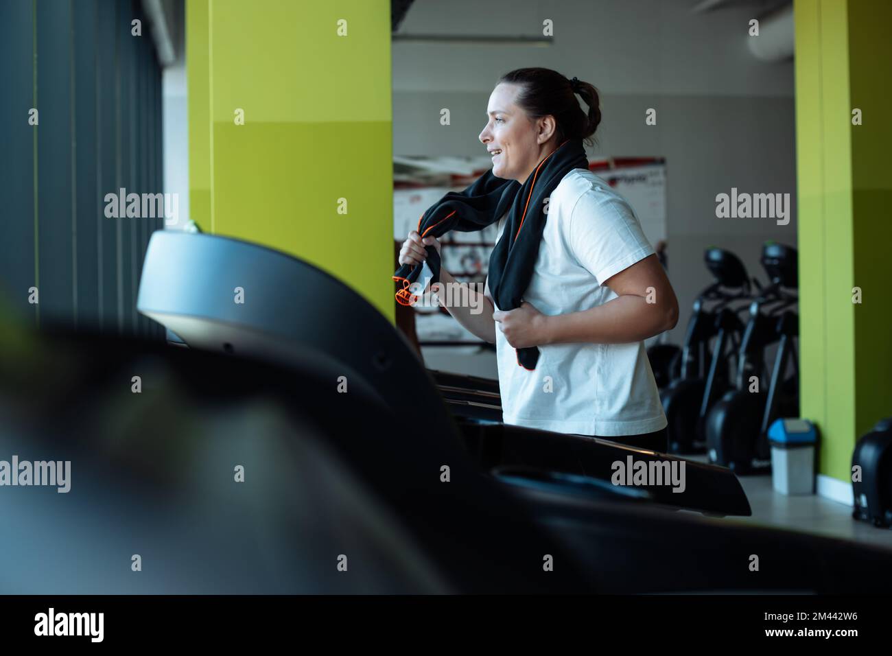 Joyful plus size woman run on modern treadmill at fitness gym, side