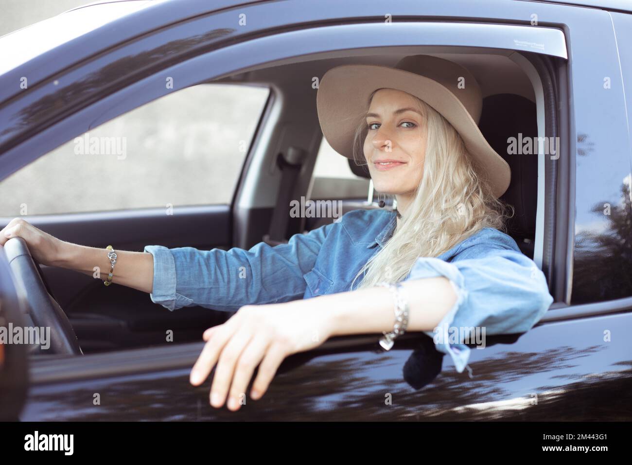 Confident smiling blond female in hat in driver seat look camera. Driving school with driving instructor. Safety on road Stock Photo