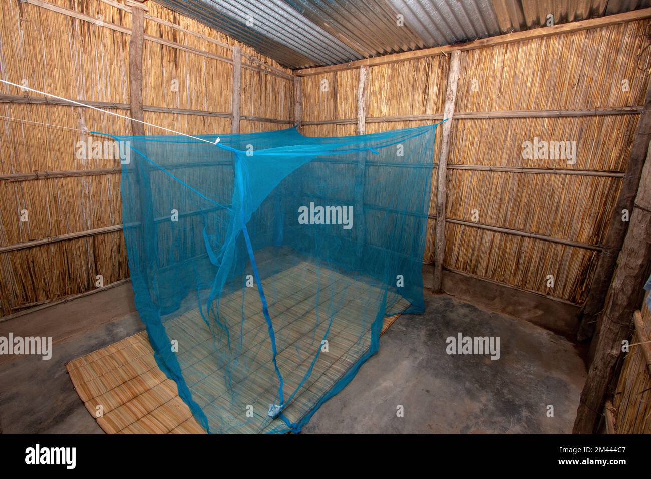 Mosquito net distributed to the community hanging in a reed house on a traditional straw mattress Stock Photo