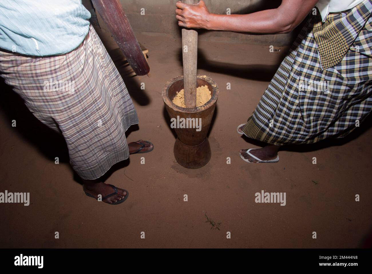 Women pounding peanuts and cassava flour in a large wooden mortar Stock Photo