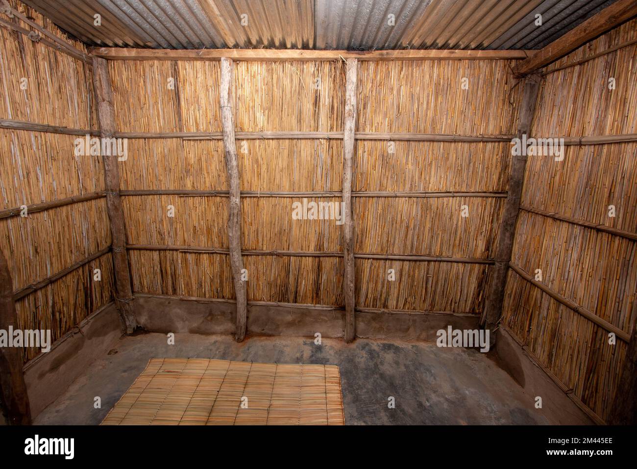 Interior view of a reed house bedroom, common in some parts of Africa, with reed walls, burnt concrete floors and zinc sheet roof Stock Photo
