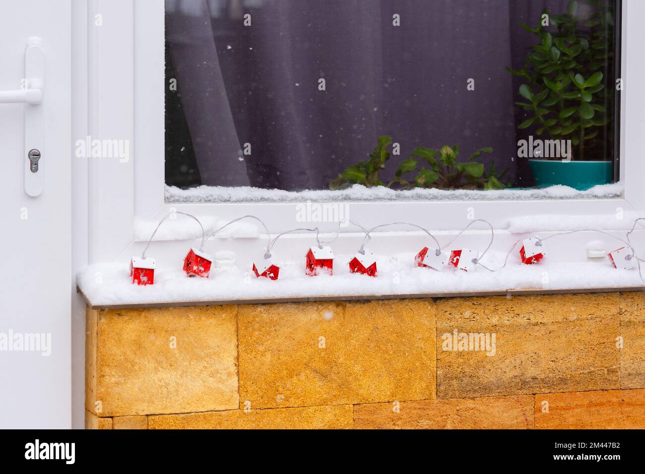 Snow garland window. Decorating the house from the outside. A red decorative wooden garland lies in the snow. The concept of an approaching holiday, N Stock Photo