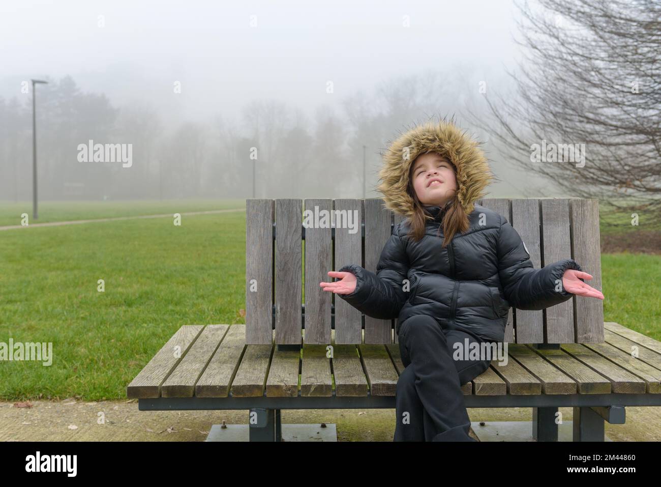 Enjoying a winter walk in the park. Teenage girl on a bench in cold weather in a warm jacket Stock Photo