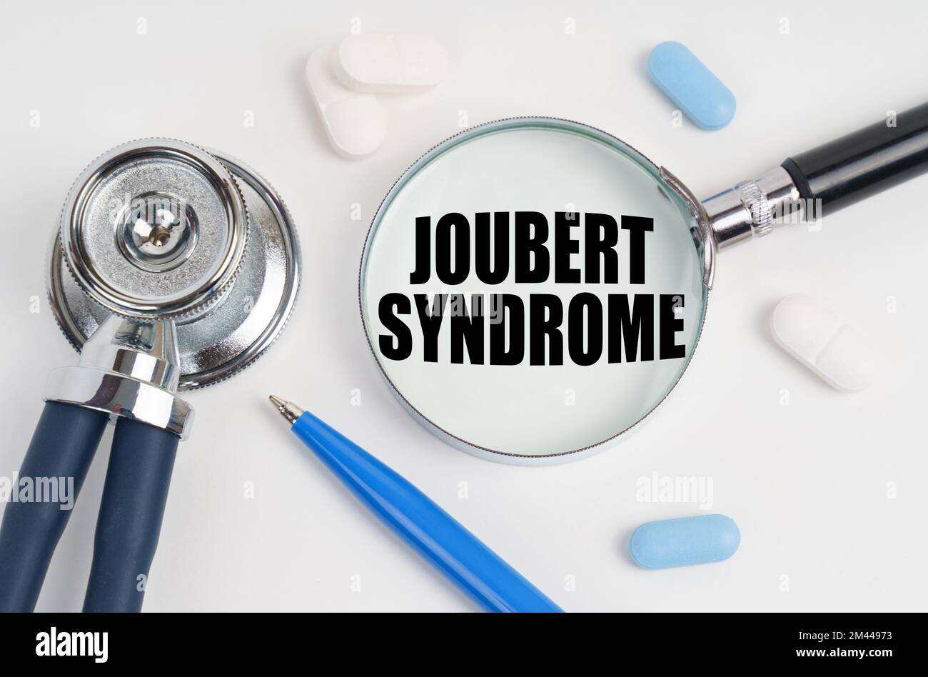 Medicine and health concept. On a white surface lie pills, a pen, a stethoscope and a magnifying glass with the inscription - Joubert syndrome Stock Photo