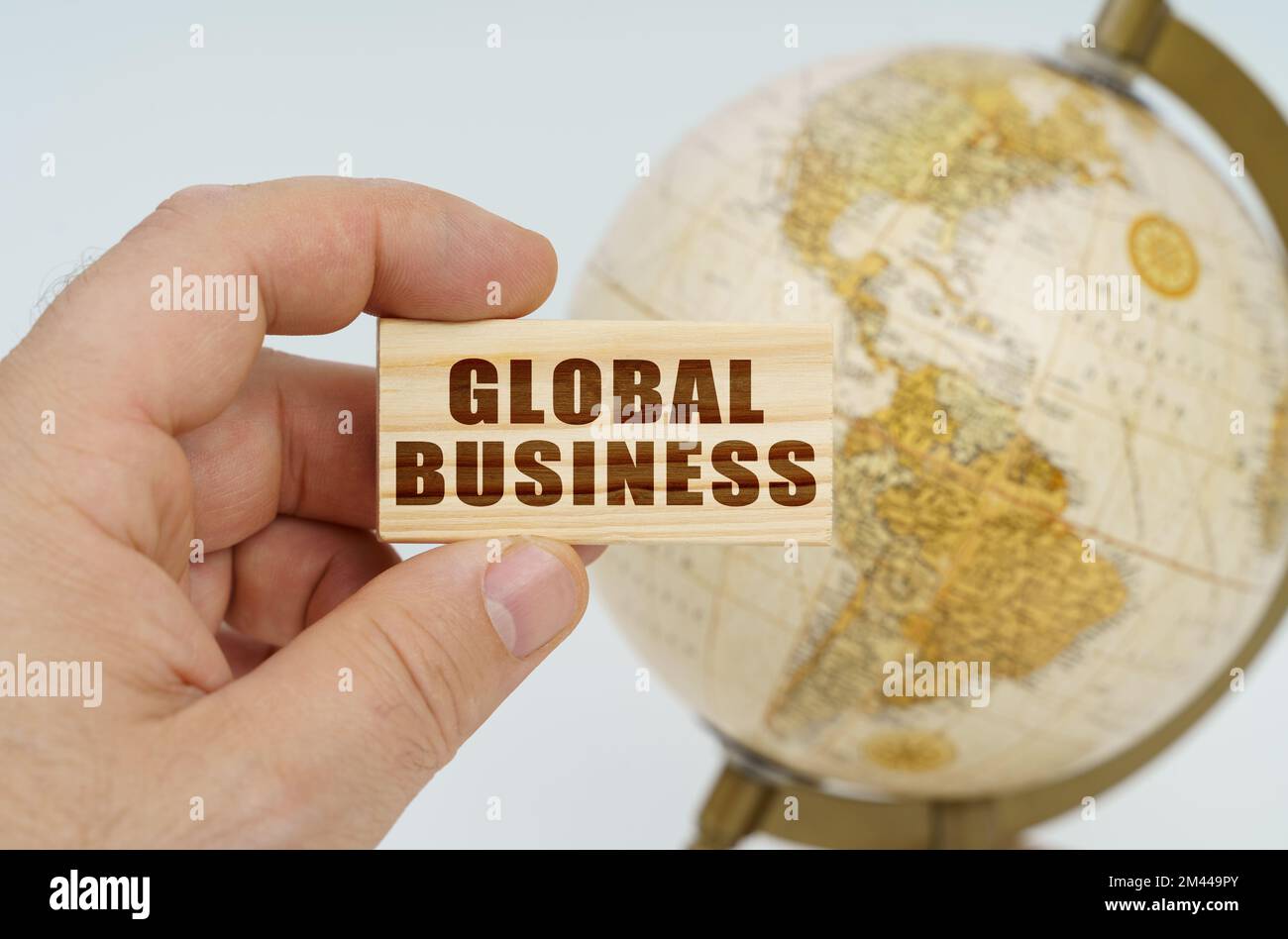 Globalization concept. A man holds in his hand a wooden plate on which it is written - GLOBAL BUSINESS. In the background is a globe. Stock Photo