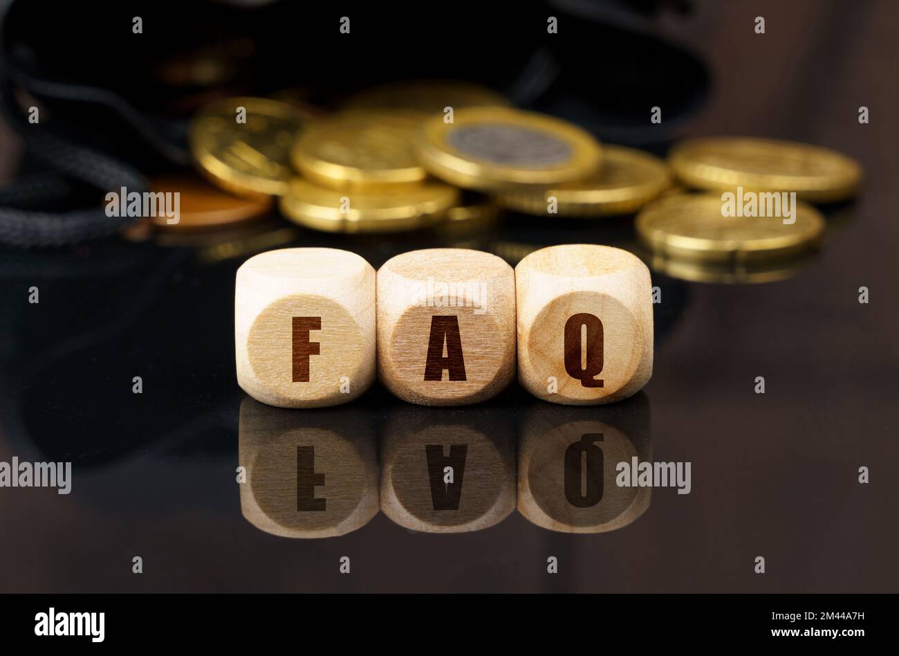 Business and economy concept. On a black reflective surface are coins and wooden cubes with the inscription - FAQ Stock Photo