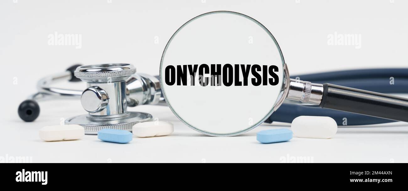Medicine and health concept. On a white surface are pills, a stethoscope and a magnifying glass inside which is written - Onycholysis Stock Photo