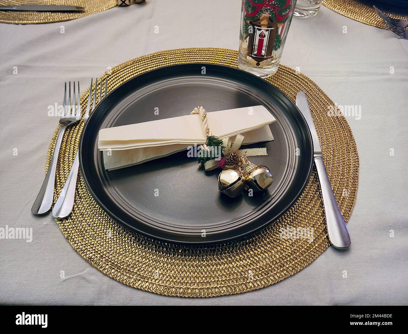 Gold Christmas bells on a black dinner plate setting with a gold