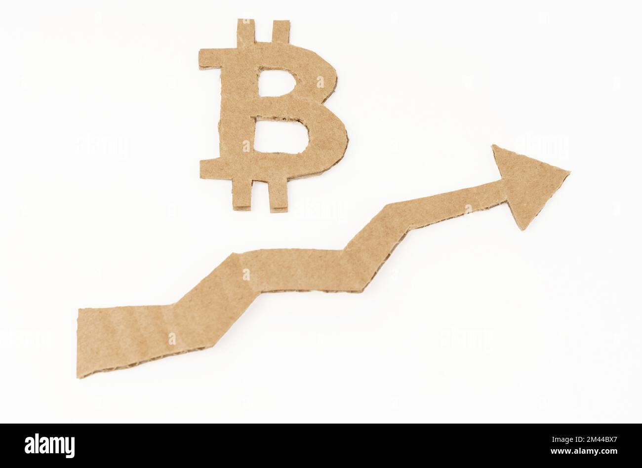 The concept of economic growth. On a white surface, a graph with an up arrow and a bitcoin symbol. Symbol, arrow and graph are made of cardboard Stock Photo