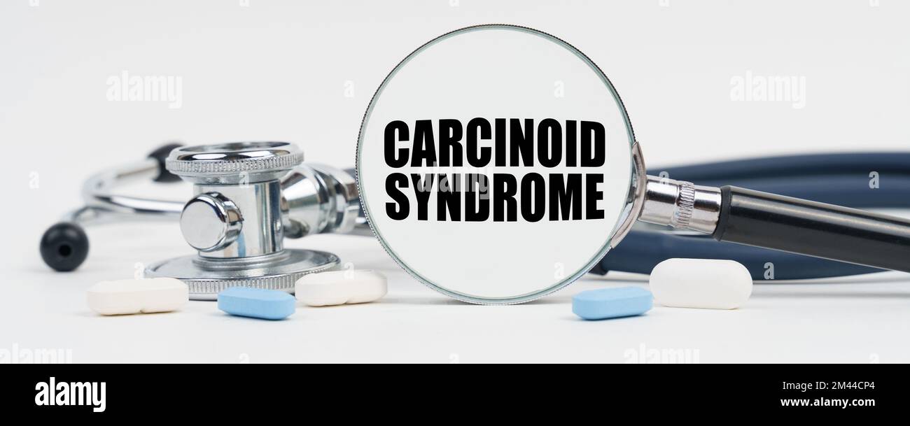 Medicine and health concept. On a white surface are pills, a stethoscope and a magnifying glass inside which is written - Carcinoid syndrome Stock Photo