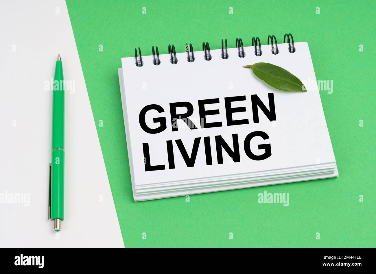 Ecological concept. On a white-green background lies a pen and a notepad with the inscription - Green Living. There is a green leaf of a plant on the Stock Photo